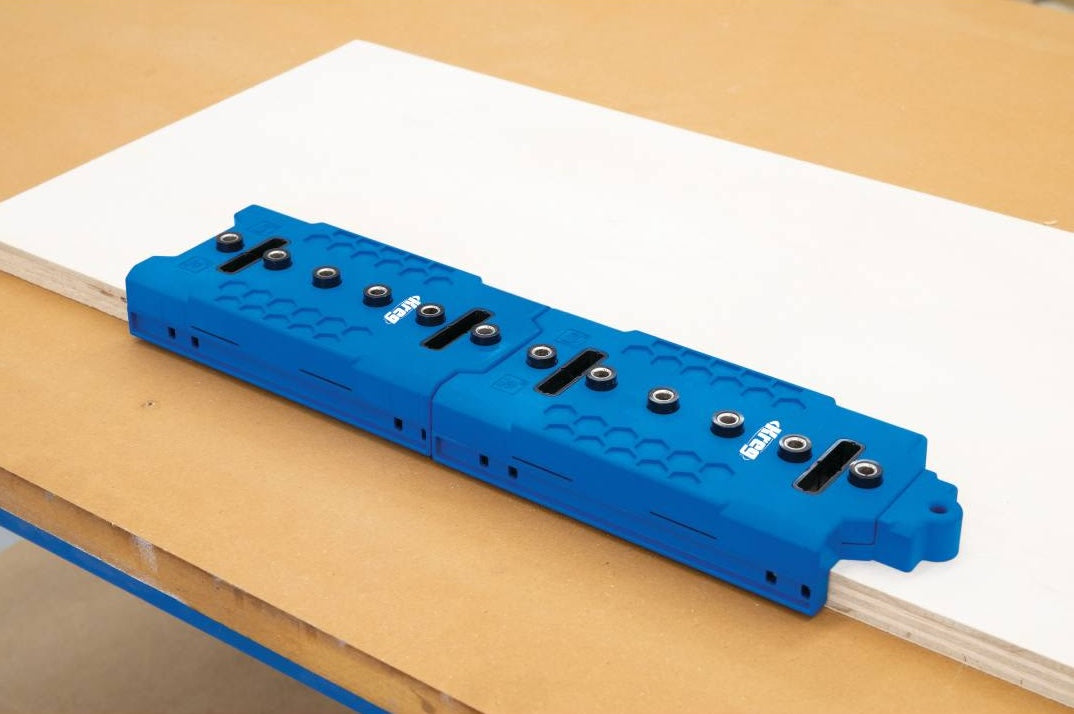 Blue plastic woodworking shelf pin jig with metal guides positioned on plywood for home improvement projects