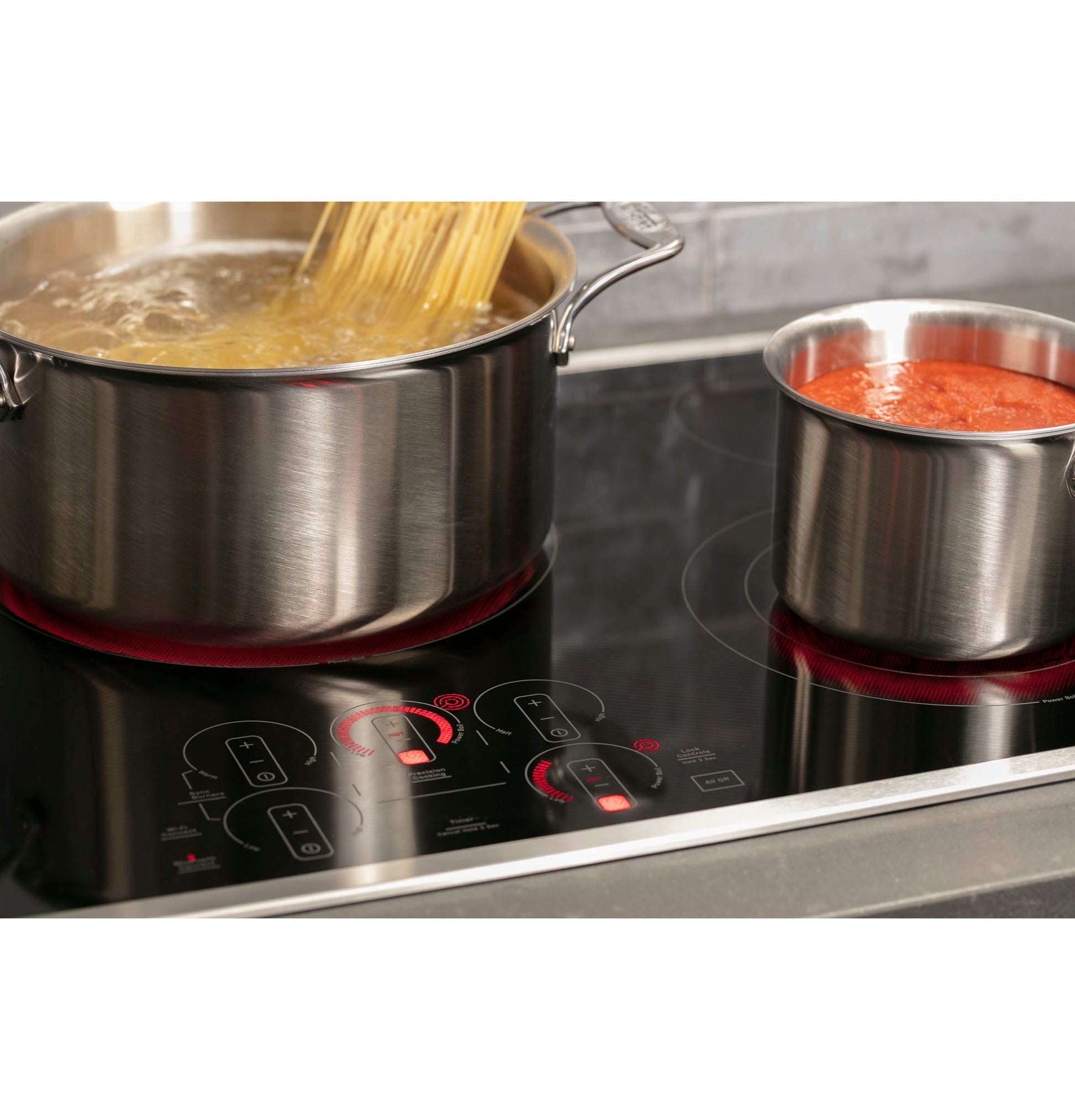 Stainless steel pots cooking pasta and sauce on active heating zones of black glass touch control electric cooktop