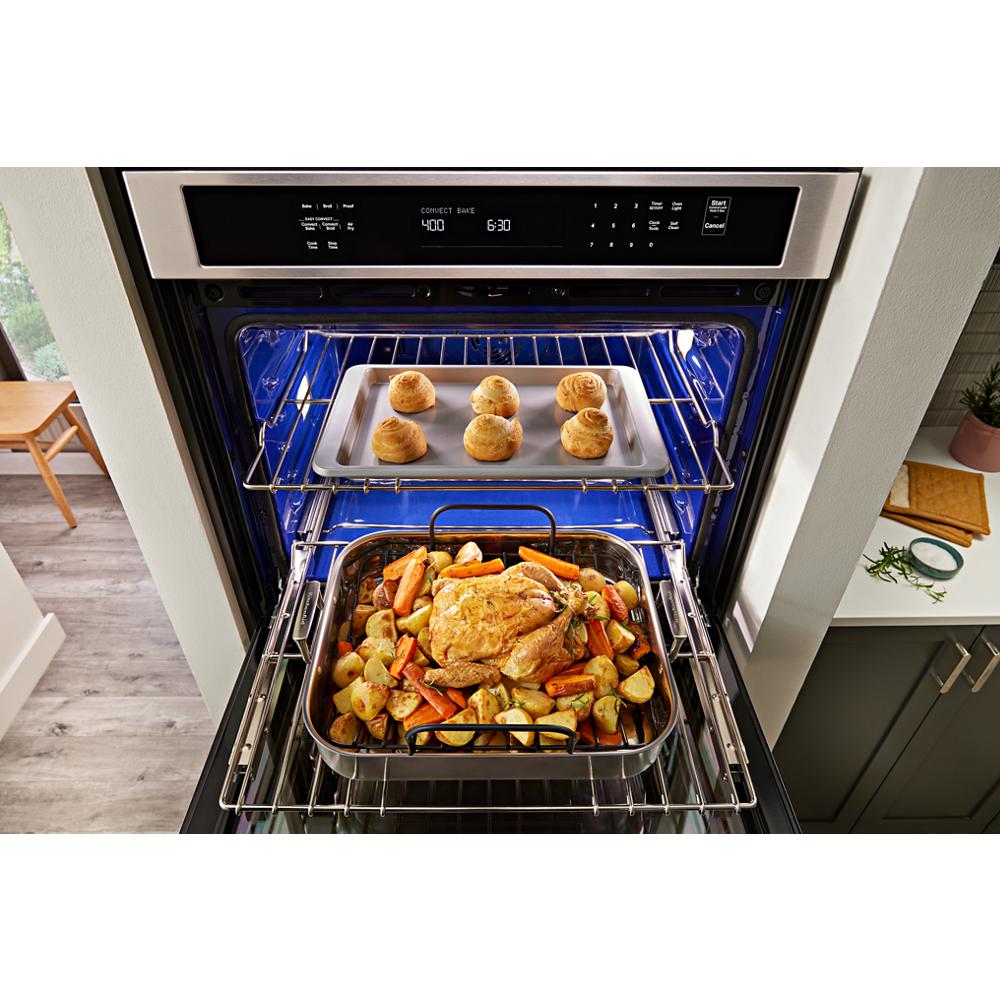 Open stainless steel wall oven with air fry basket roasting chicken and vegetables and baking bread rolls inside