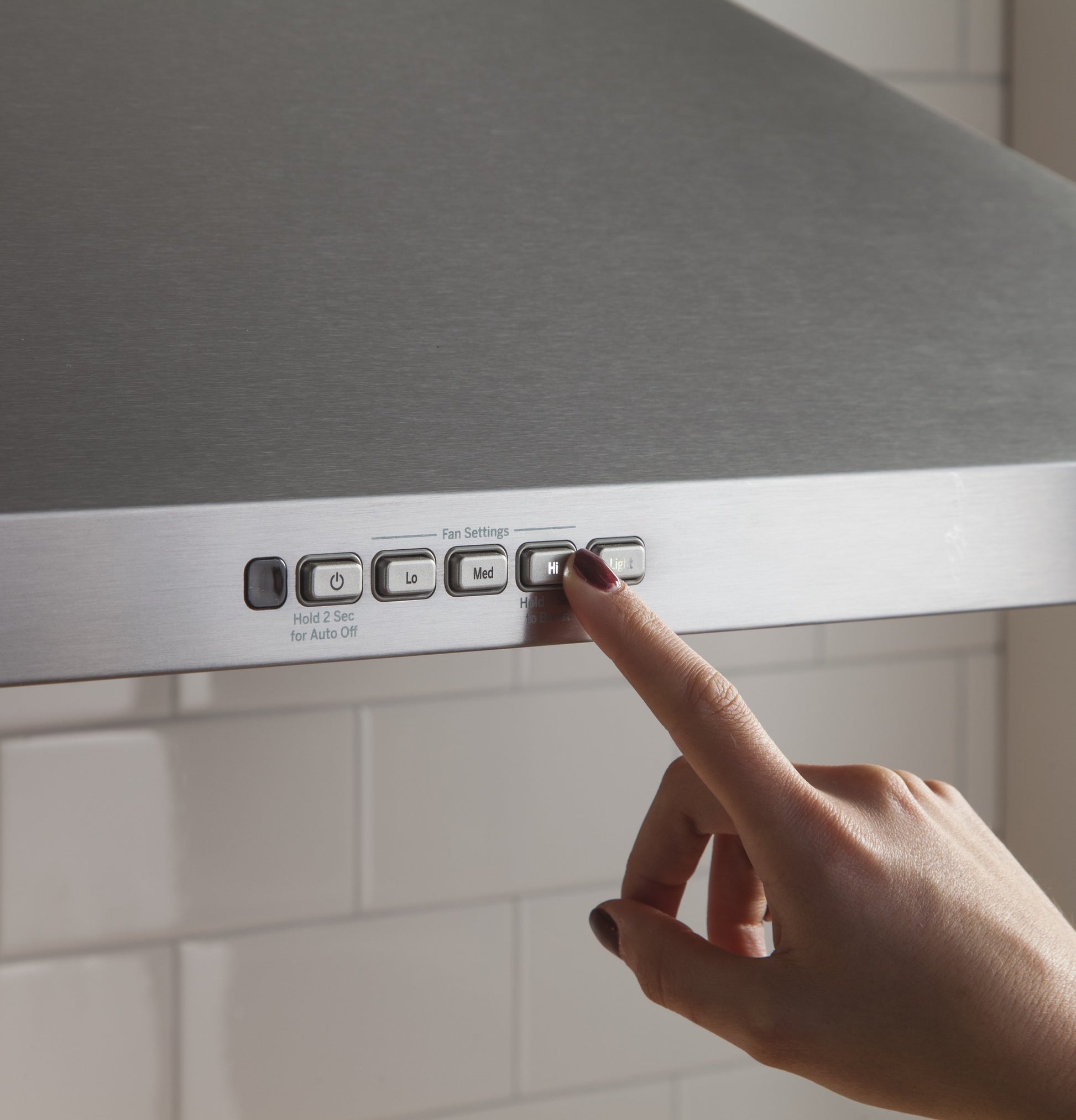 Finger pressing high fan speed button on stainless steel wall-mount pyramid chimney hood from Range Hoods collection
