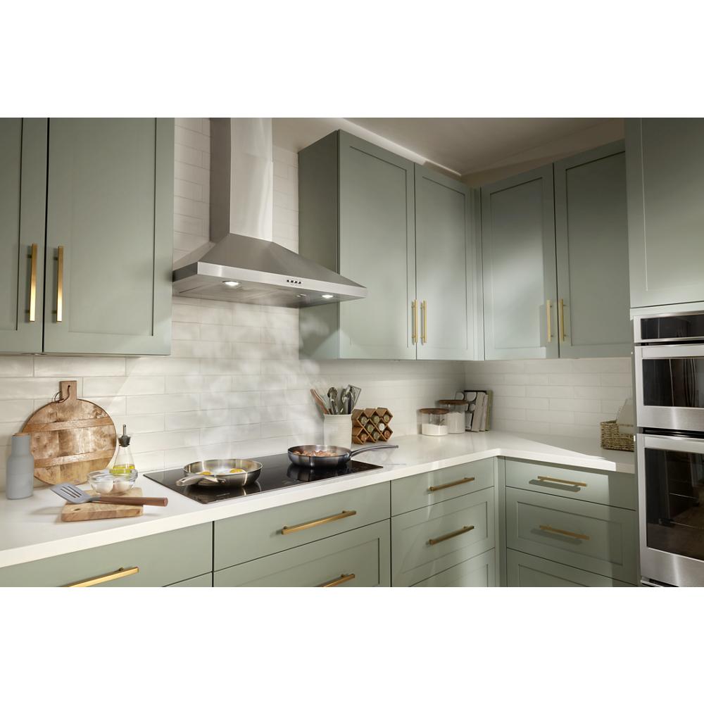 Modern kitchen featuring a stainless steel chimney wall mount hood above stovetop with sage green cabinets and gold hardware