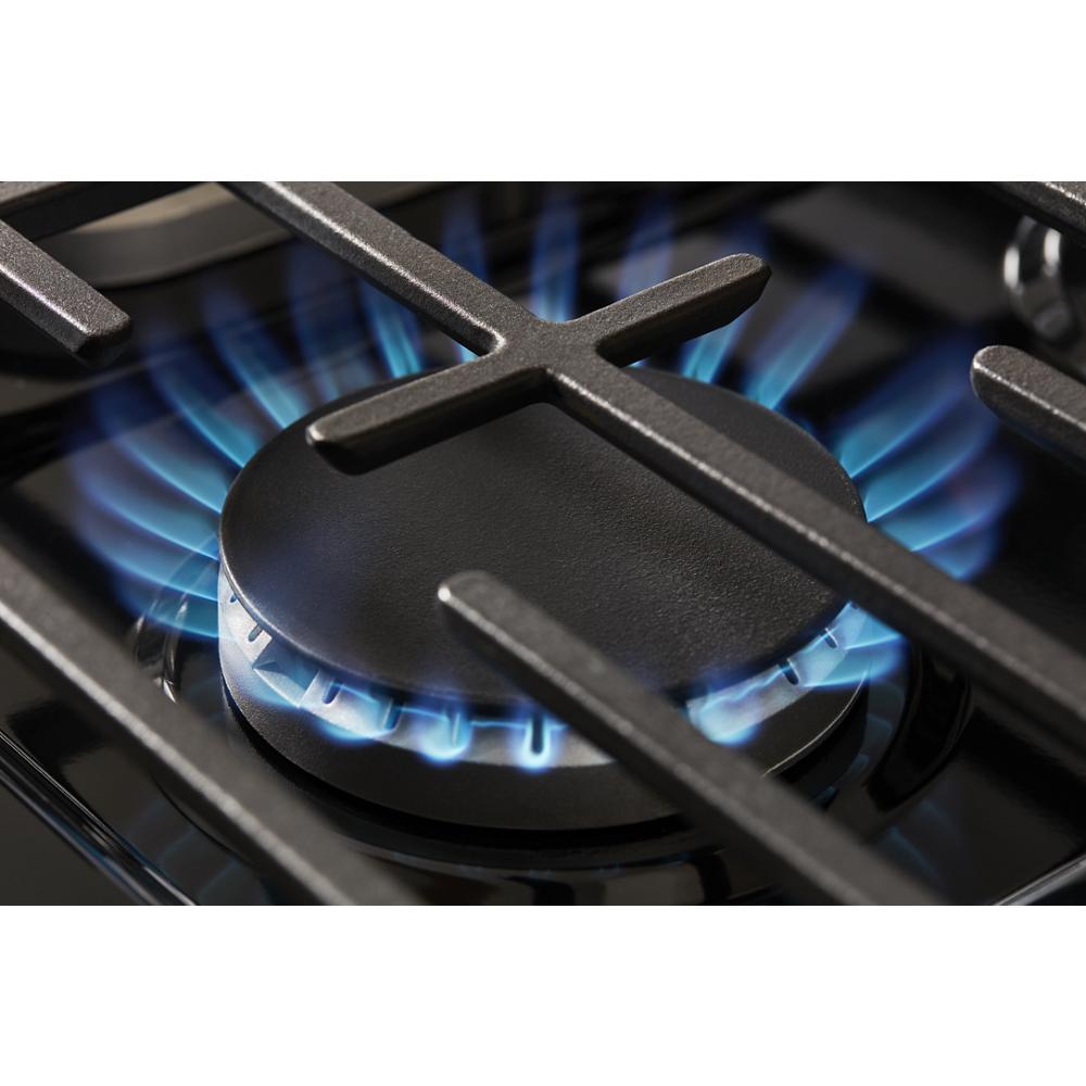 Close-up of blue flame burning on a burner of a freestanding gas range with cast-iron grates in kitchen appliances.