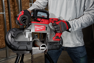Person wearing gloves operating a Milwaukee portable band saw cutting metal pipe in a workshop setting