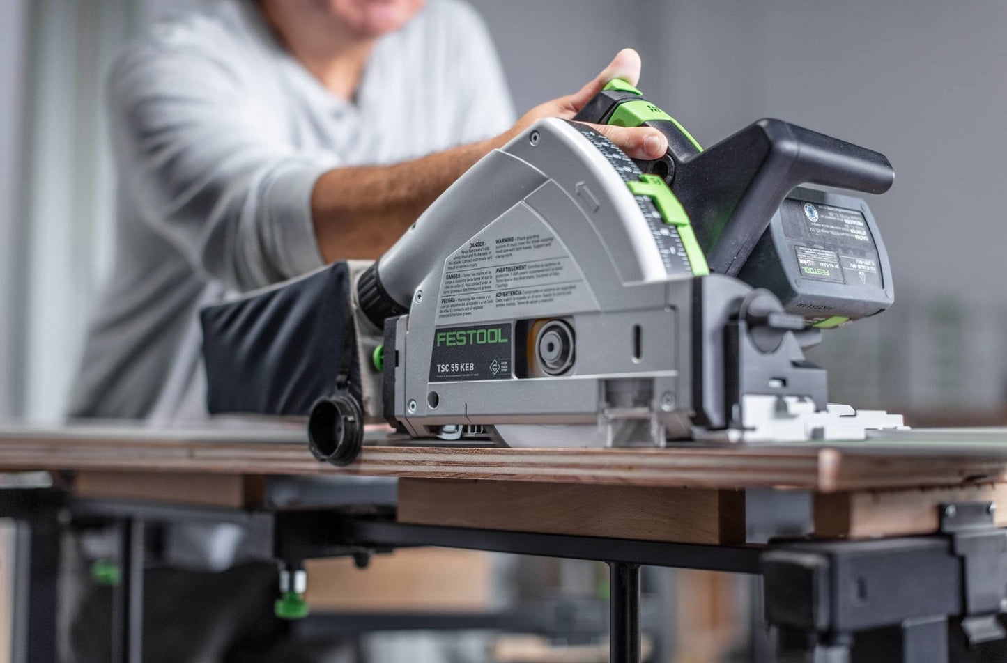 Person operating a Festool cordless track saw with guide rail cutting wood on a workbench in power tools collection