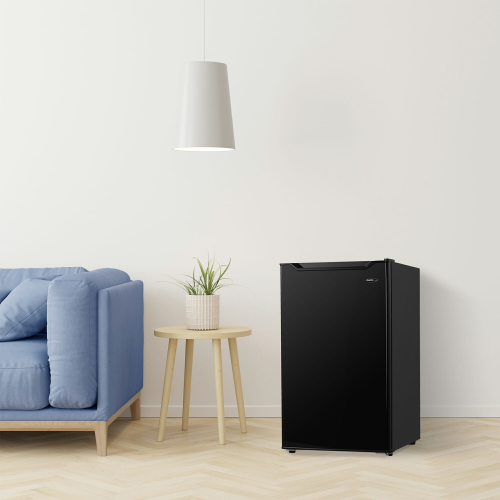 Compact black refrigerator with smooth finish placed beside wooden side table and blue sofa in modern living space