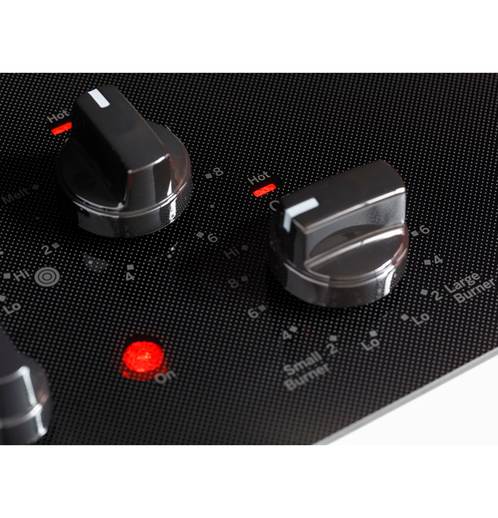 Close-up of black knob controls on GE® electric cooktop with illuminated red indicator lights in kitchen setting