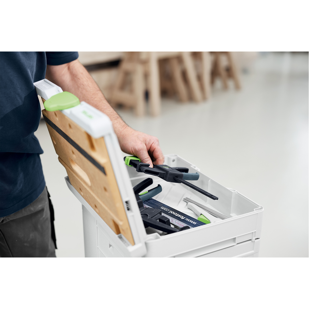 Person placing a clamp inside an open white storage box with a wooden lid, part of an interlocking system for organizing woodworking hand tools.