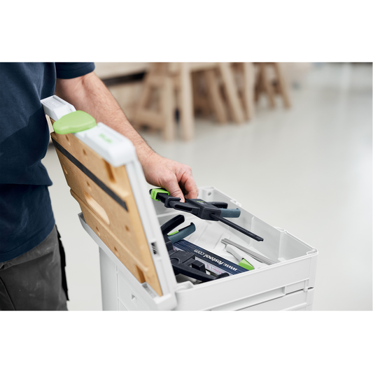 Person placing a clamp inside an open white storage box with a wooden lid, part of an interlocking system for organizing woodworking hand tools.