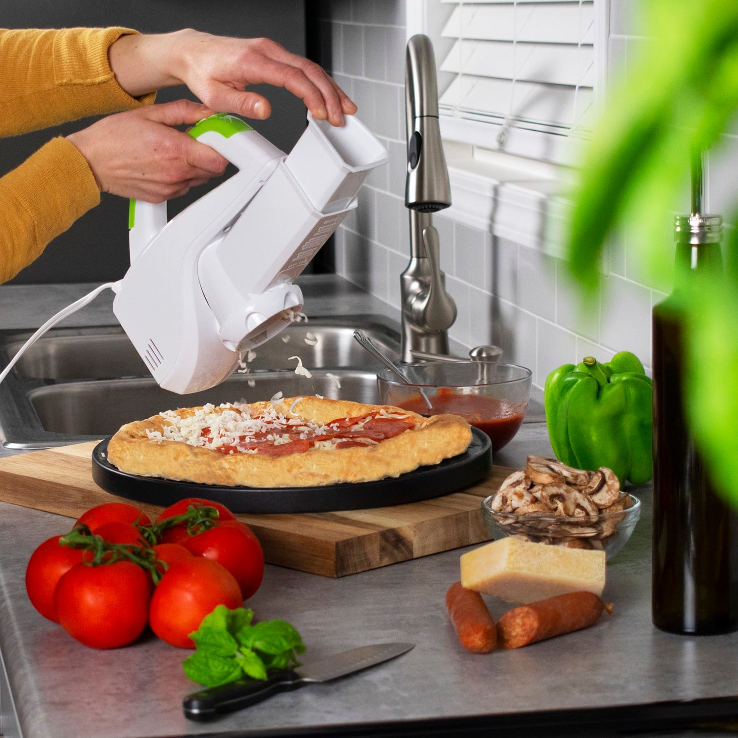 White and green electric slicer shredding cheese onto pizza crust with fresh vegetables nearby in kitchen gadgets collections
