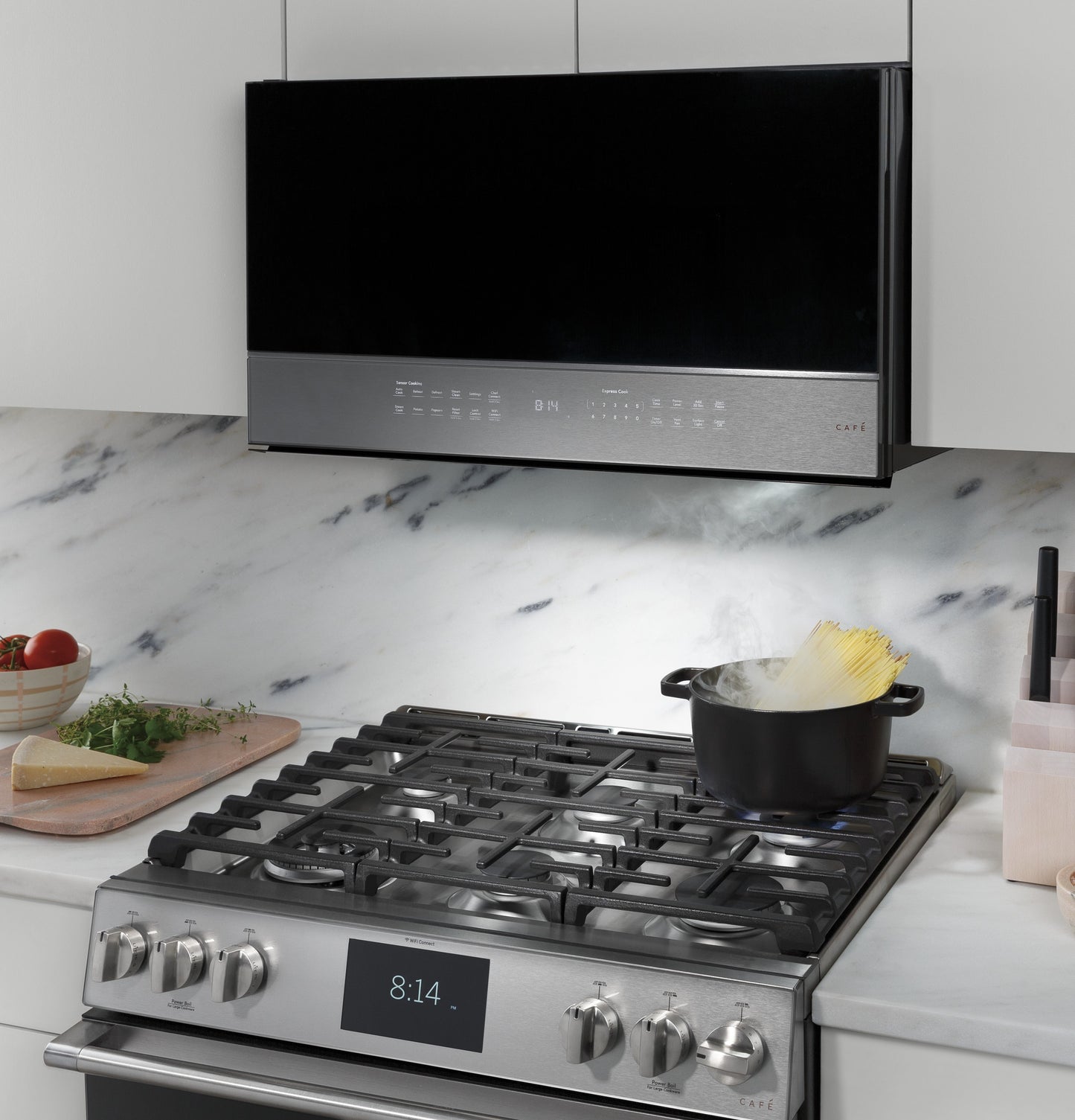 Platinum glass smart over-the-range microwave installed above a gas cooktop with a steaming pot of pasta in kitchen setting