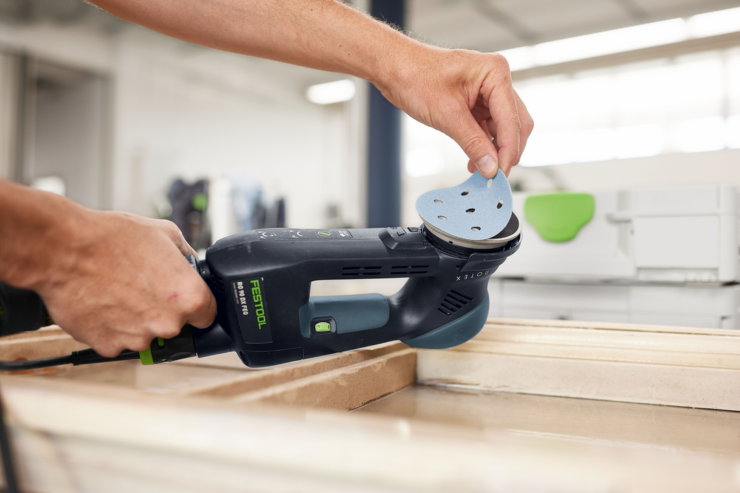 Person attaching blue sanding disc to Festool sander for woodworking in power tool accessories and abrasives collections