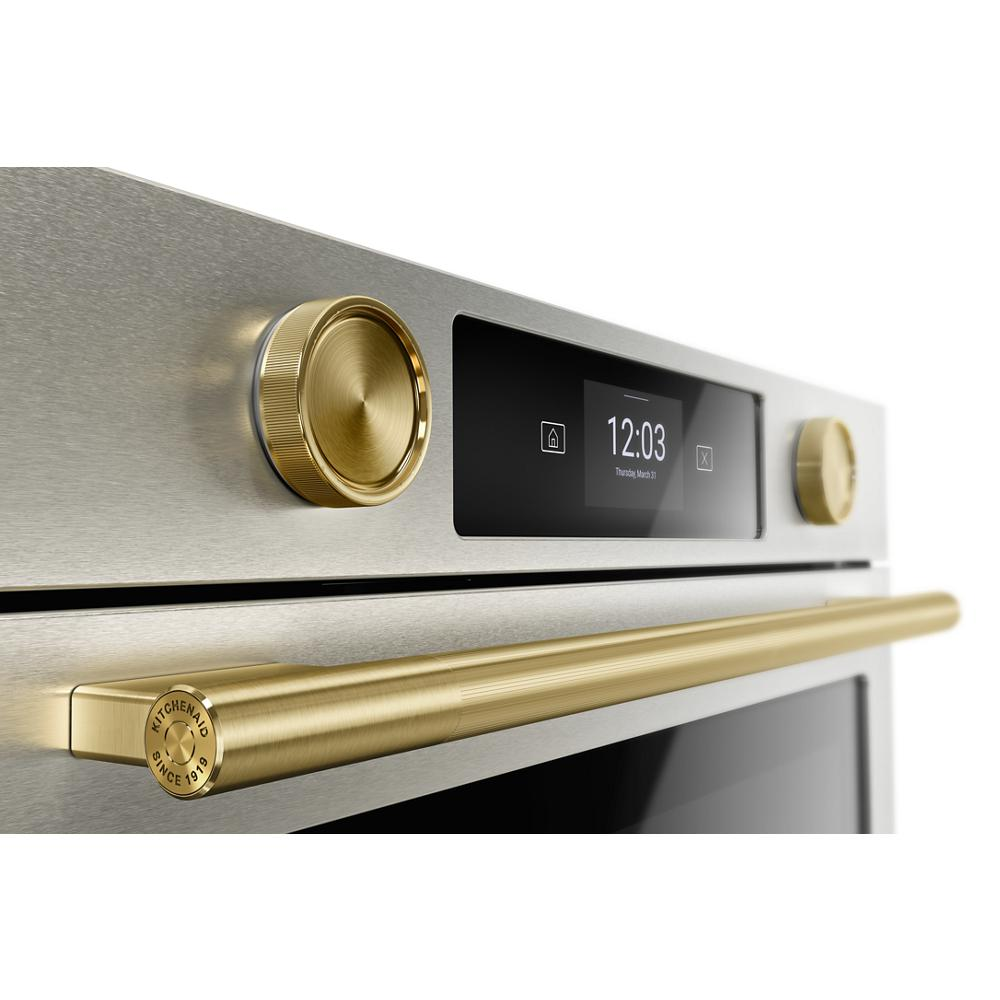 Close-up of brushed gold knobs and handle on stainless steel smart electric wall oven with digital LED display