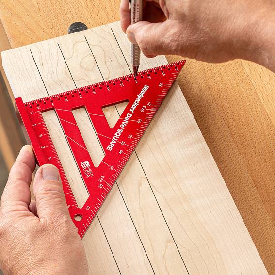 Red measuring triangle with precise scales being used to mark straight lines on smooth light wood for woodworking tasks