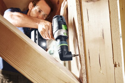 Worker wearing safety glasses using Festool cordless hammer drill on wooden beams for home improvement tasks