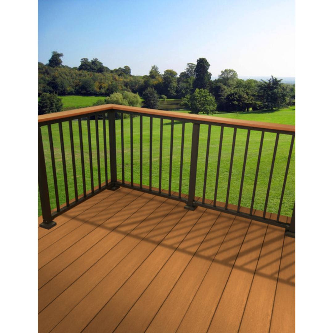 Corner view of brown composite deck flooring with black metal railing overlooking green lawn and trees
