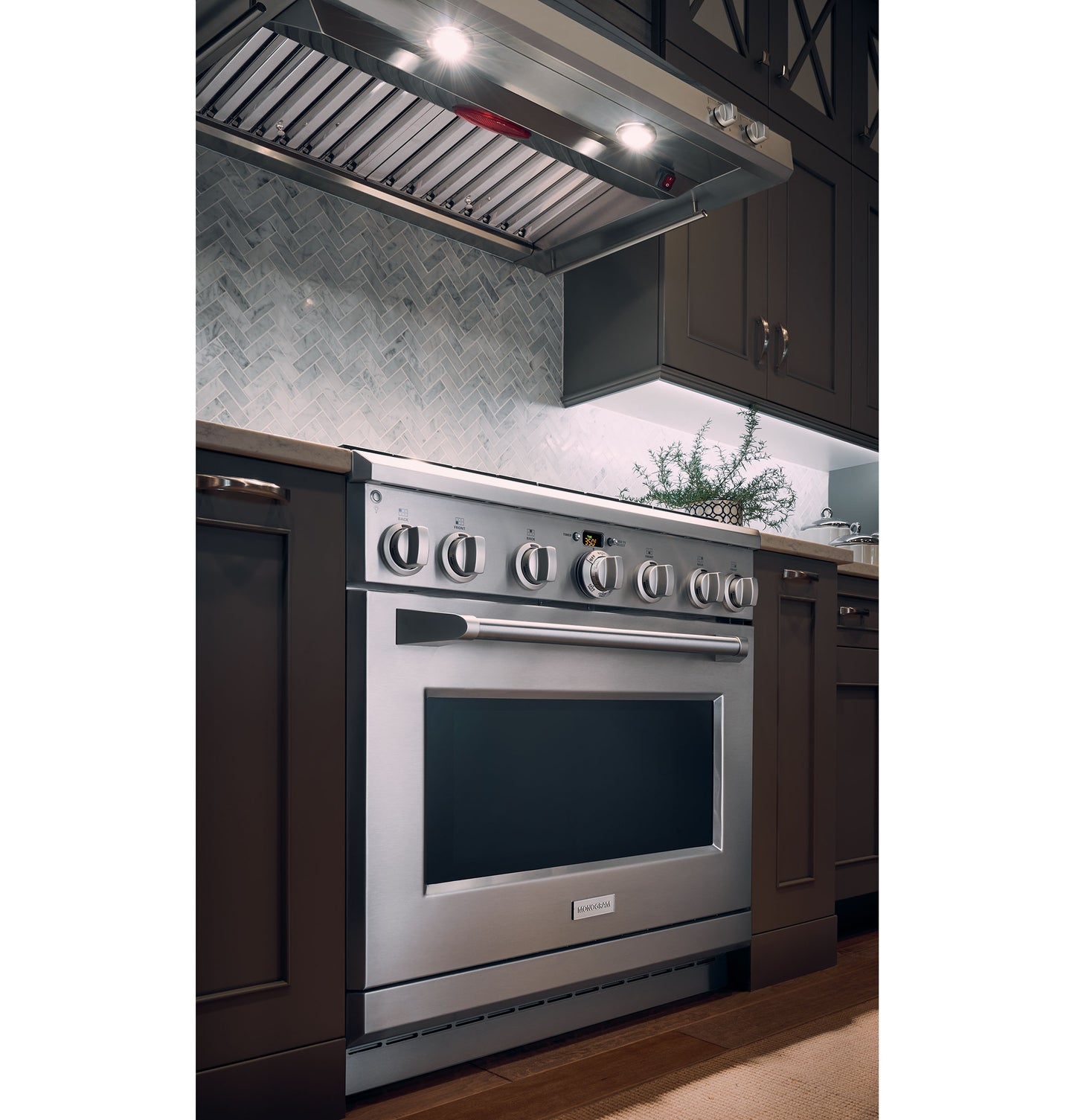 Modern kitchen with stainless steel professional range hood and gas oven surrounded by dark cabinetry and herringbone backsplash