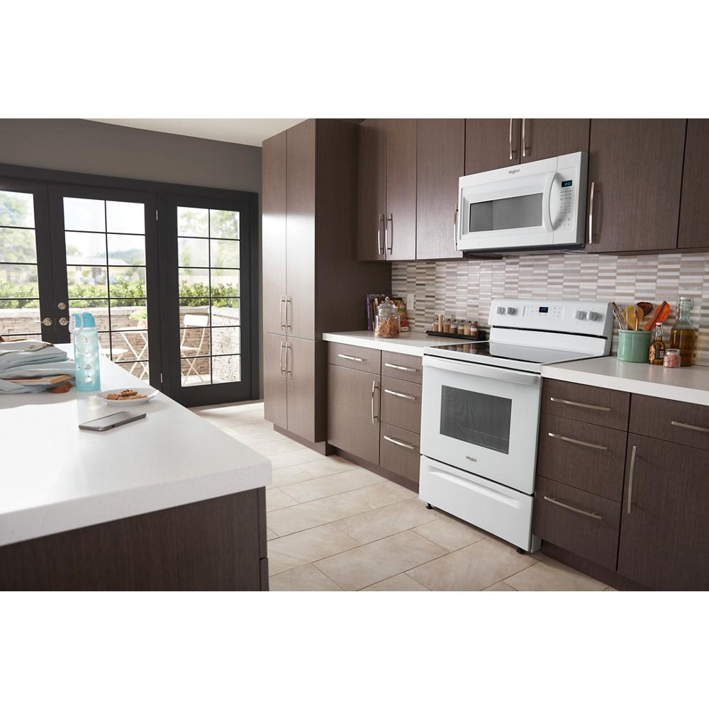 White microwave with sensor cooking technology installed above electric stove in modern kitchen with dark cabinets