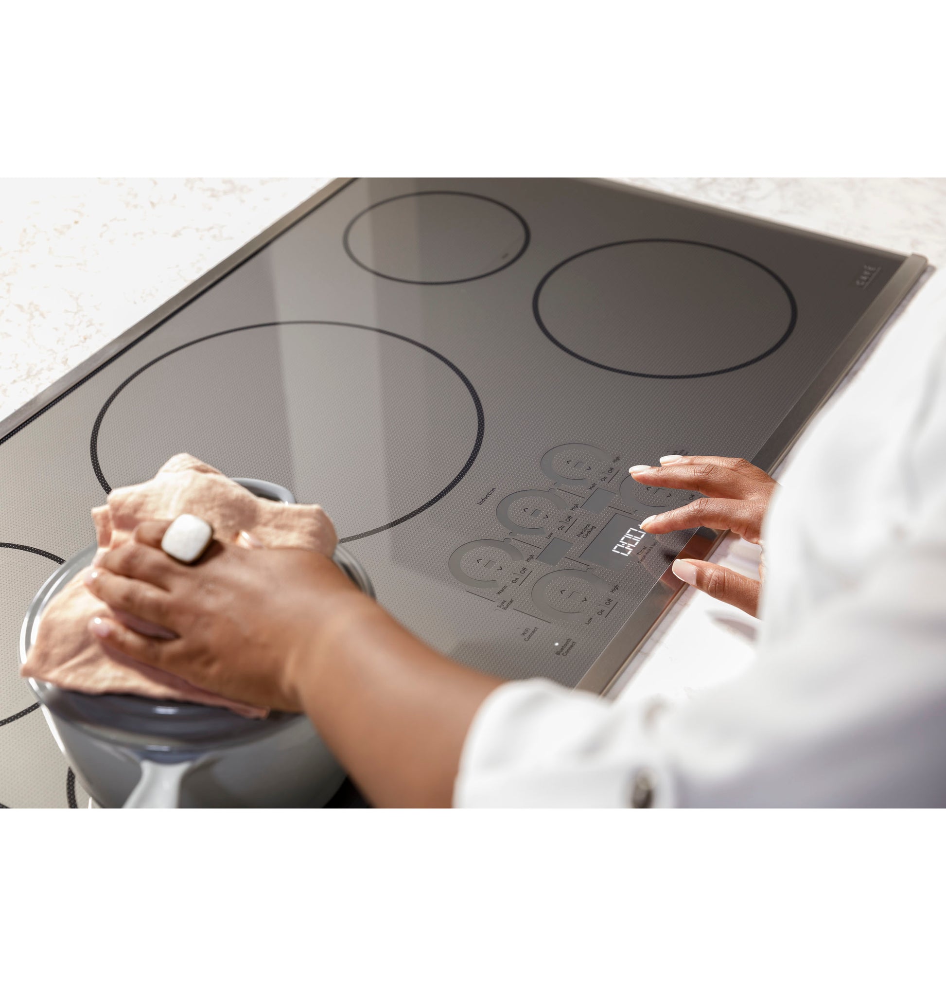 Person wiping smooth black glass surface of a built-in touch control induction cooktop in kitchen appliances collection