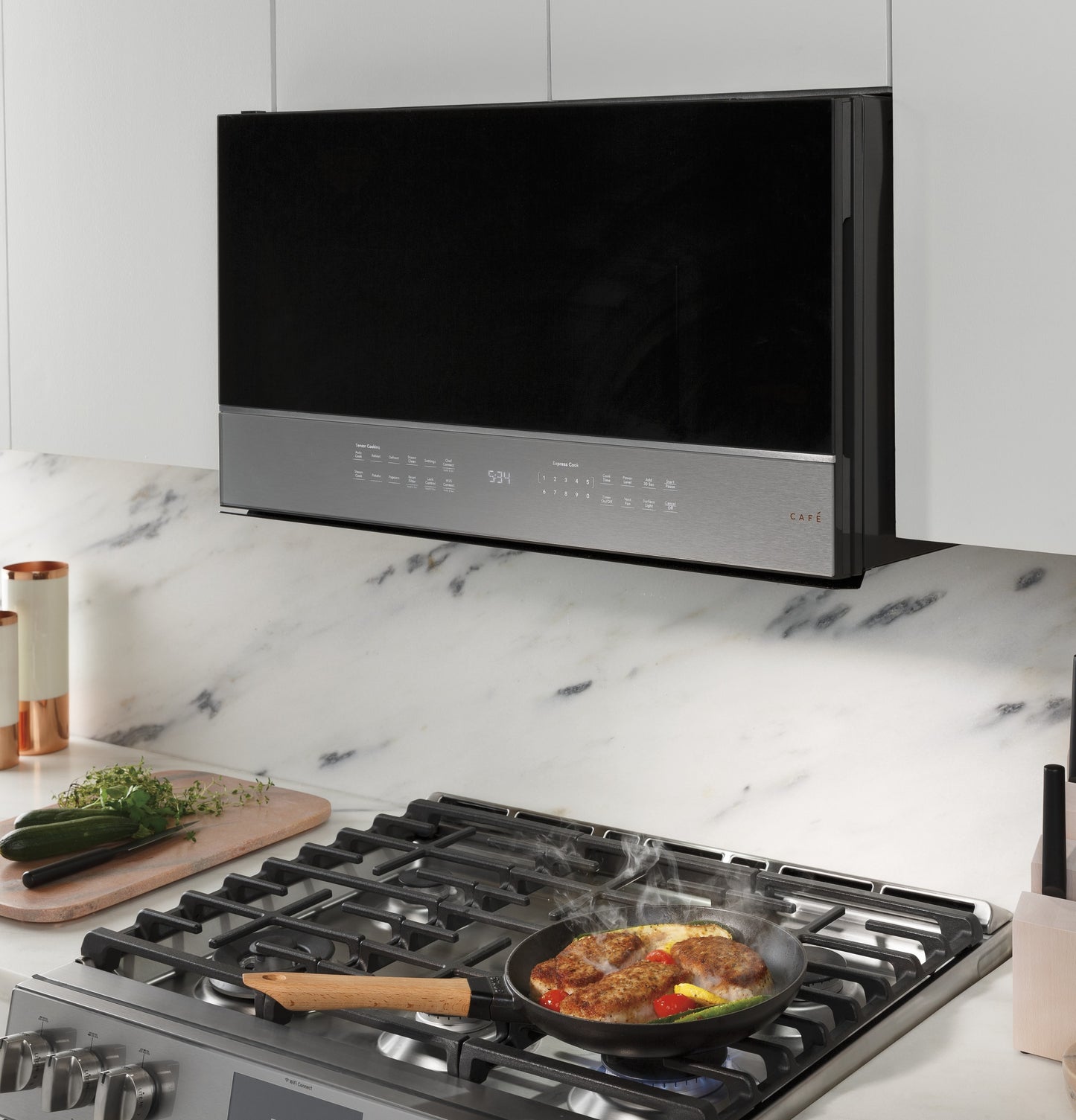 Smart over-the-range microwave in platinum glass installed above a gas stove with food cooking on burner