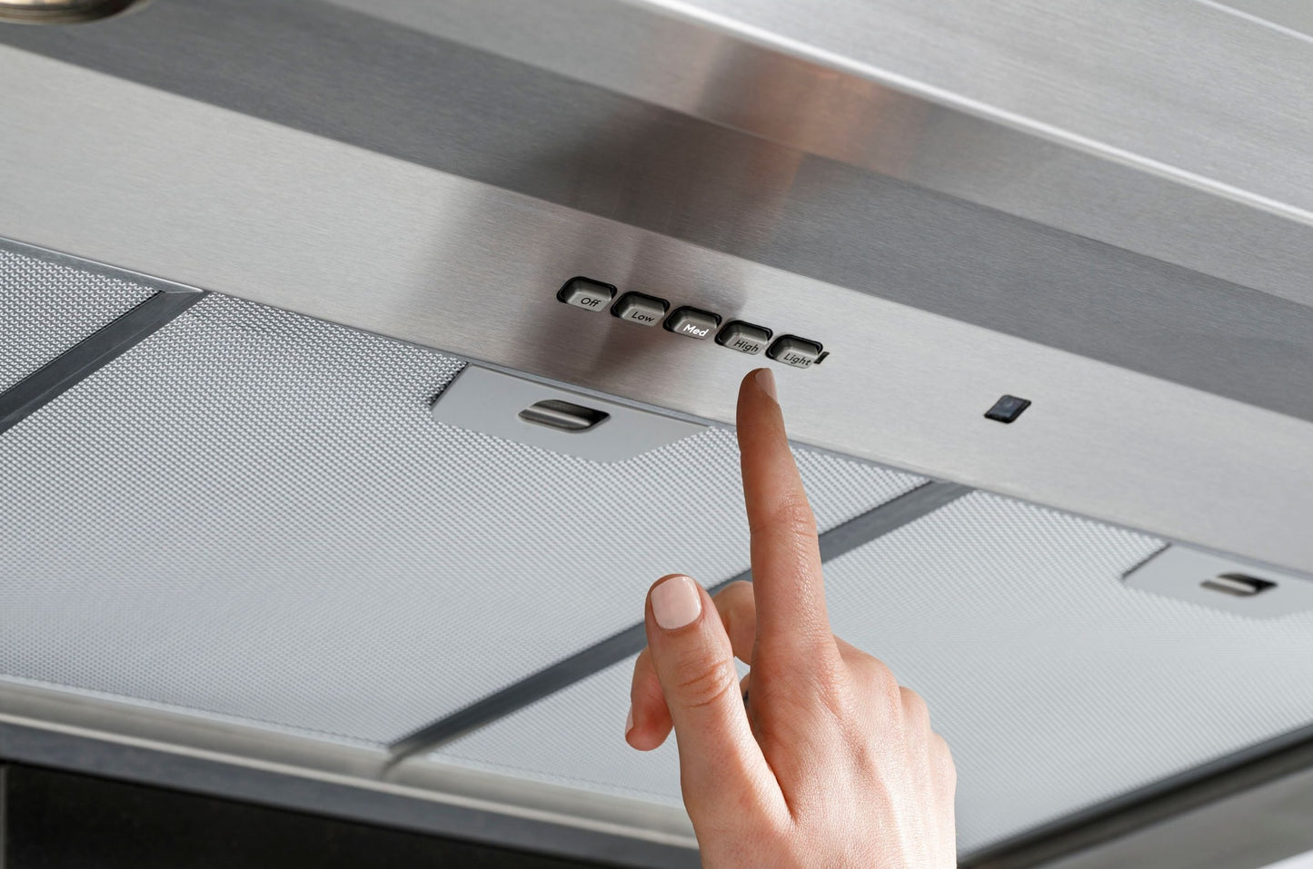 Close-up of stainless steel wall mount hood control panel with finger pressing a button in kitchen appliances collection