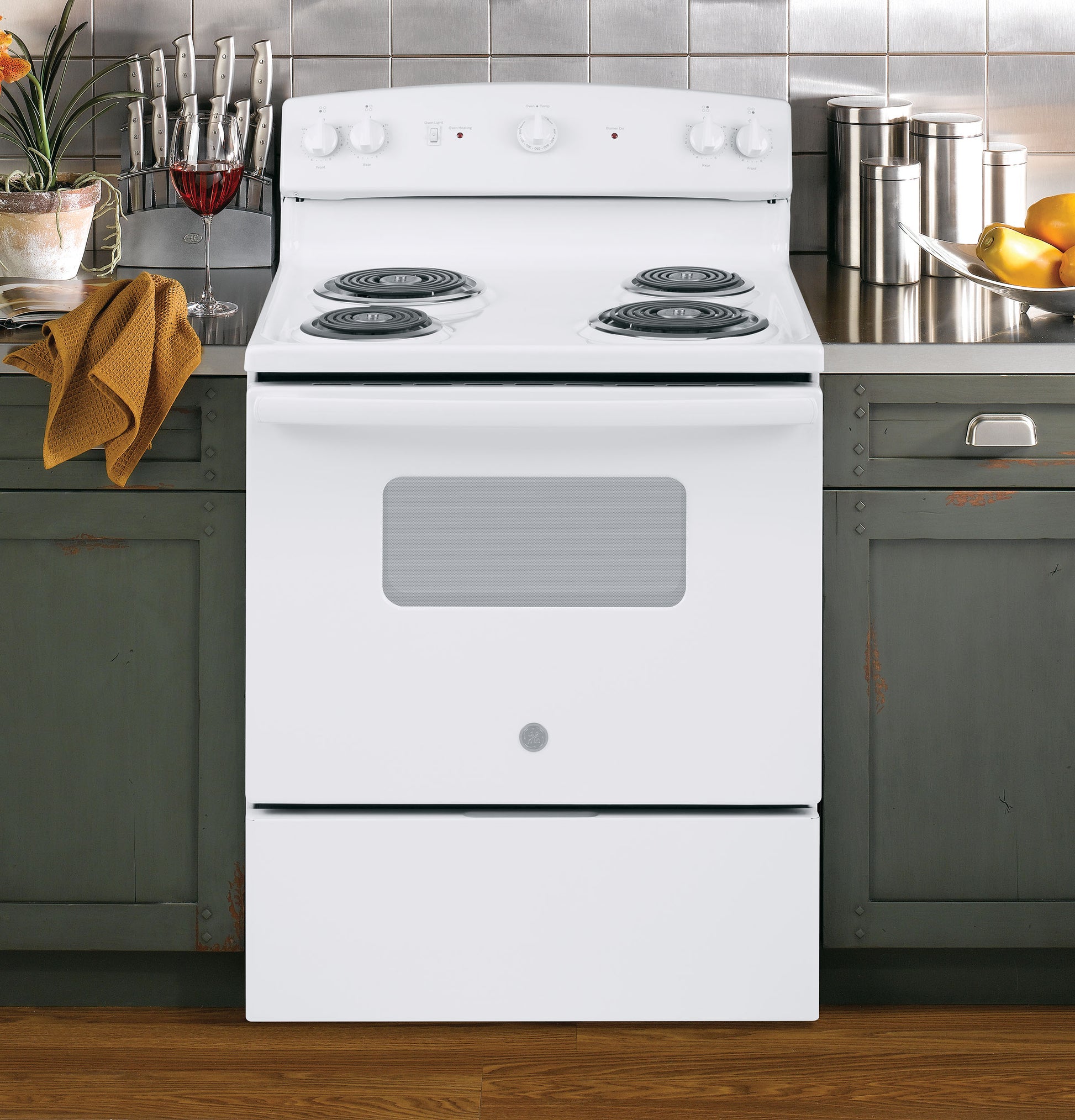 White electric range with four coil burners and oven, set in a kitchen with green cabinets and metal backsplash tiles