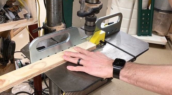 Metal drill press fence with yellow magnetic stops securing wood for precise drilling in power tool accessories collection