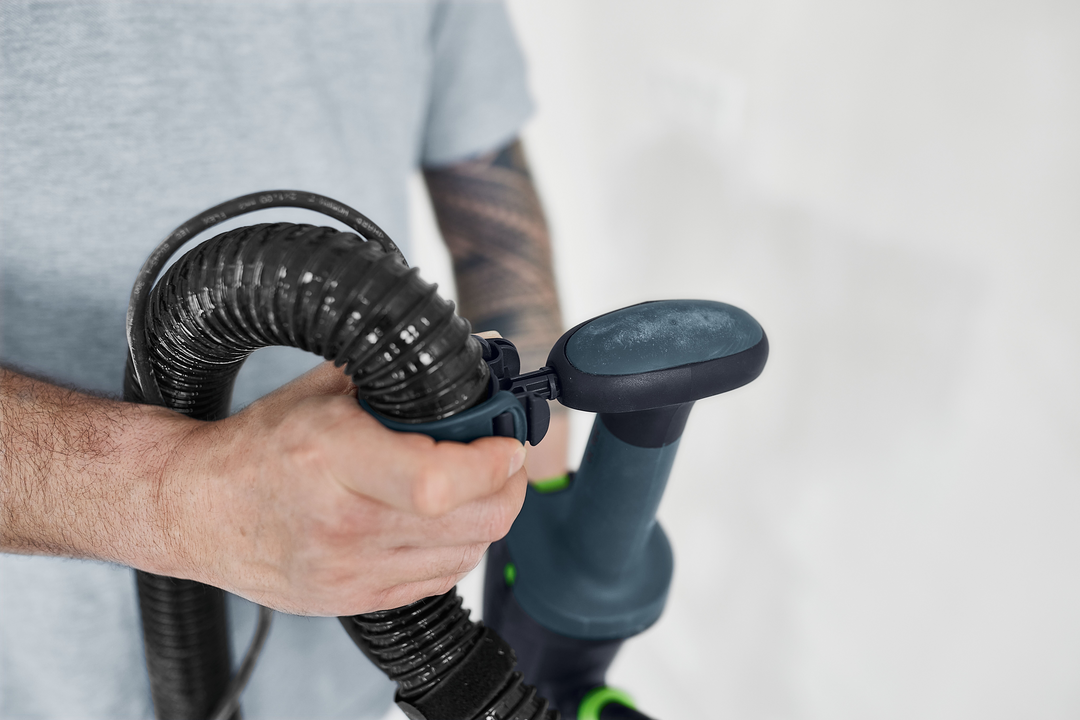 Close-up of hand gripping handle and flexible hose of Festool drywall sander in power tools and home improvement setting