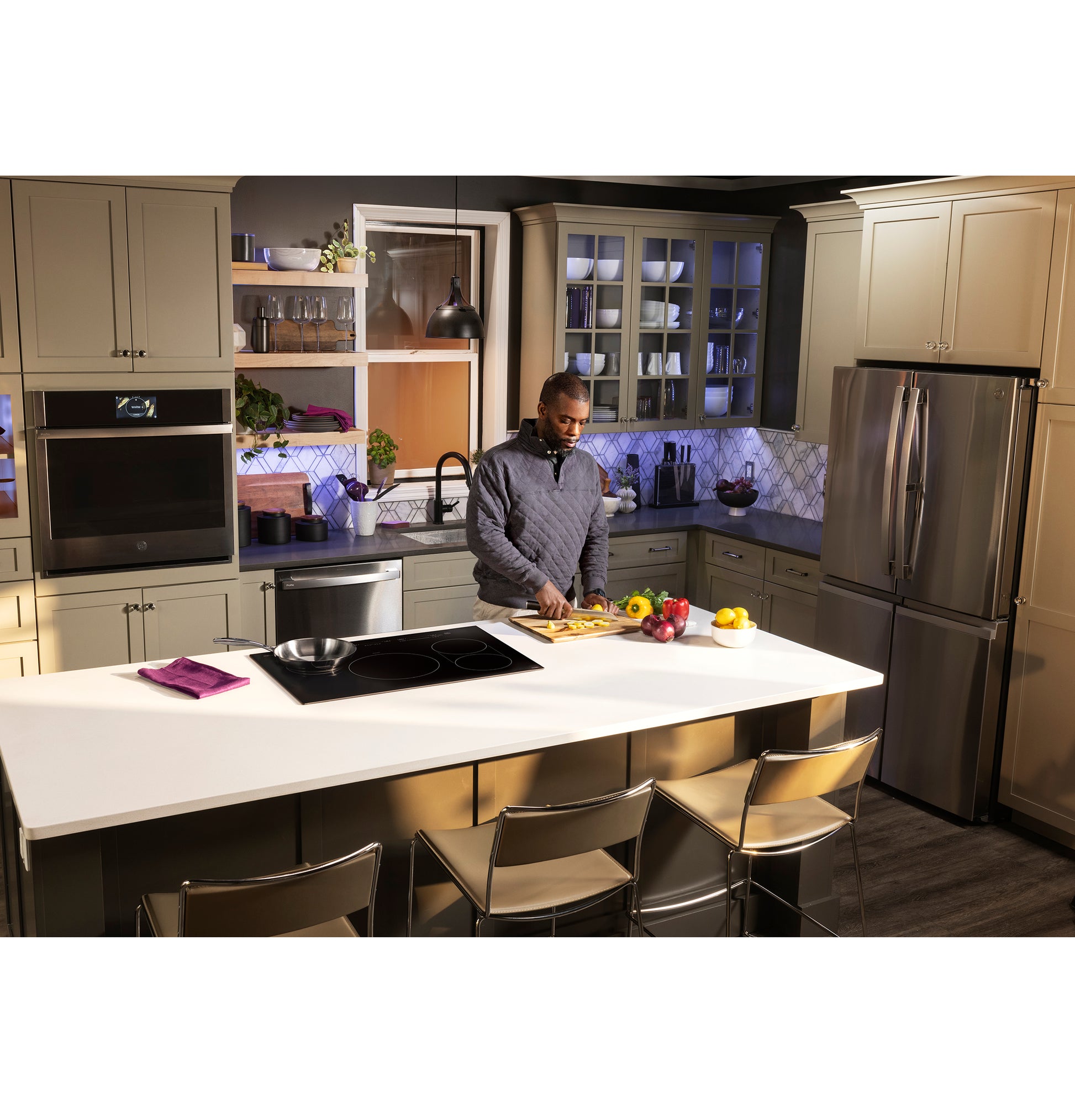 Modern kitchen scene with man chopping vegetables on island featuring built-in induction cooktop and stainless appliances