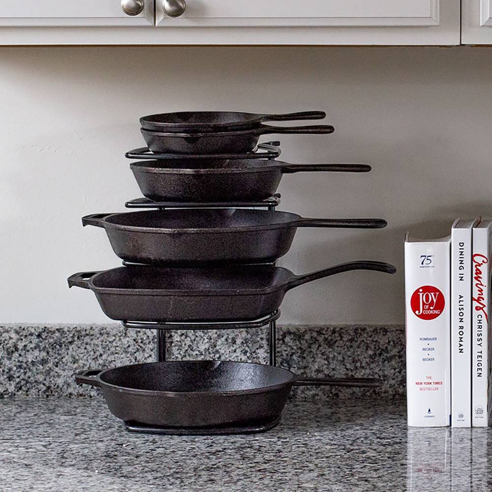 Black five-tier cast iron skillet organizer on granite countertop with stacked cookware and cookbooks nearby