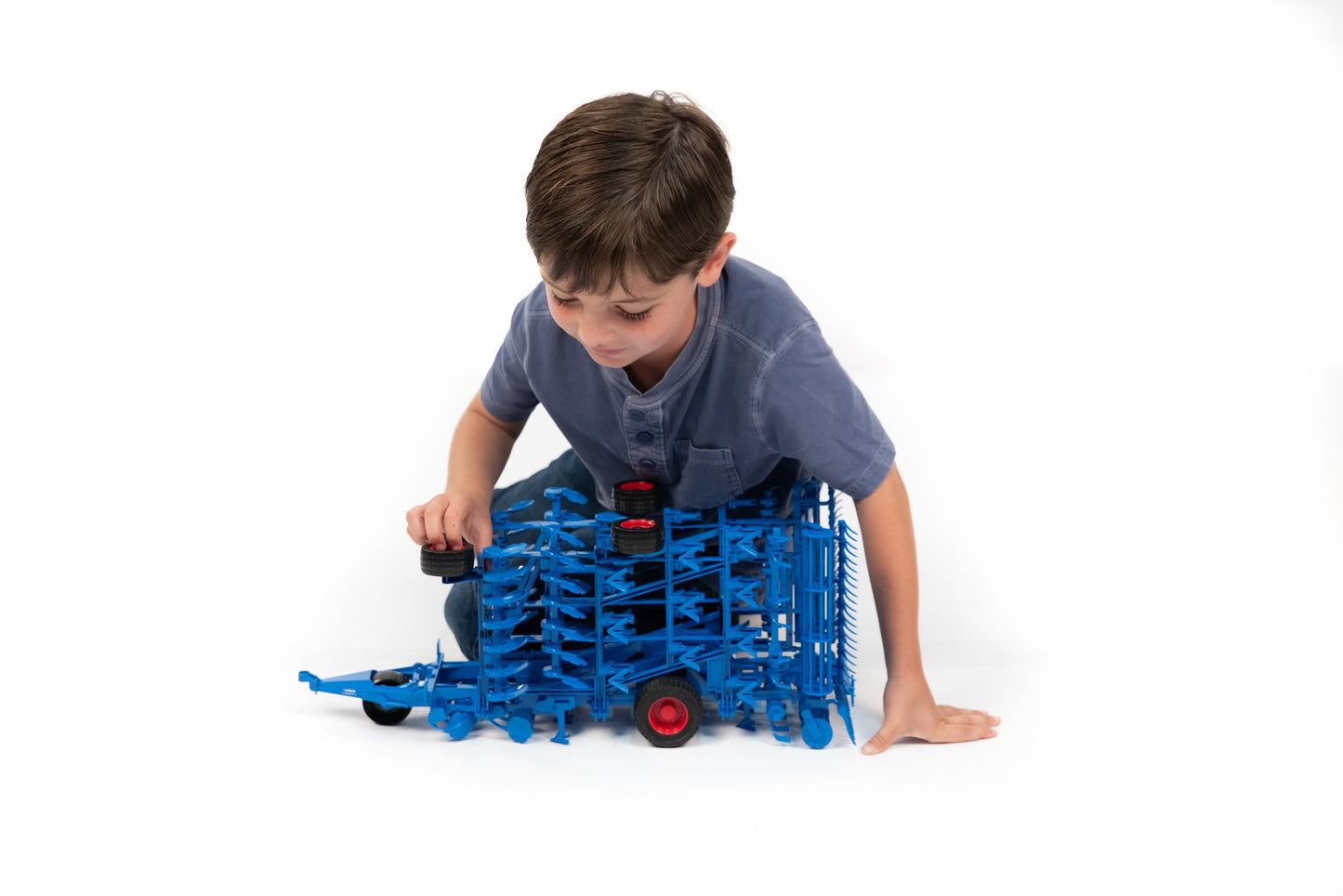 Young boy examining detailed blue toy cultivator model for tools and home improvement play activities