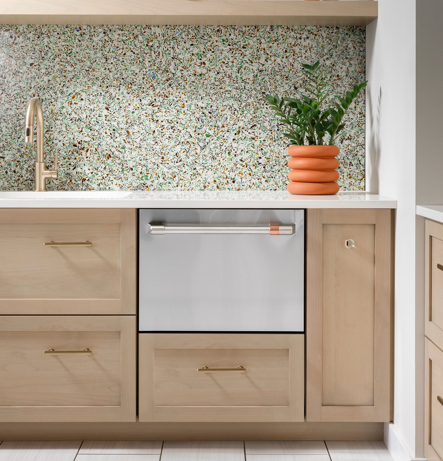 Built-in stainless steel dishwasher drawer integrated into light wood kitchen cabinetry with terrazzo backsplash and plant decor