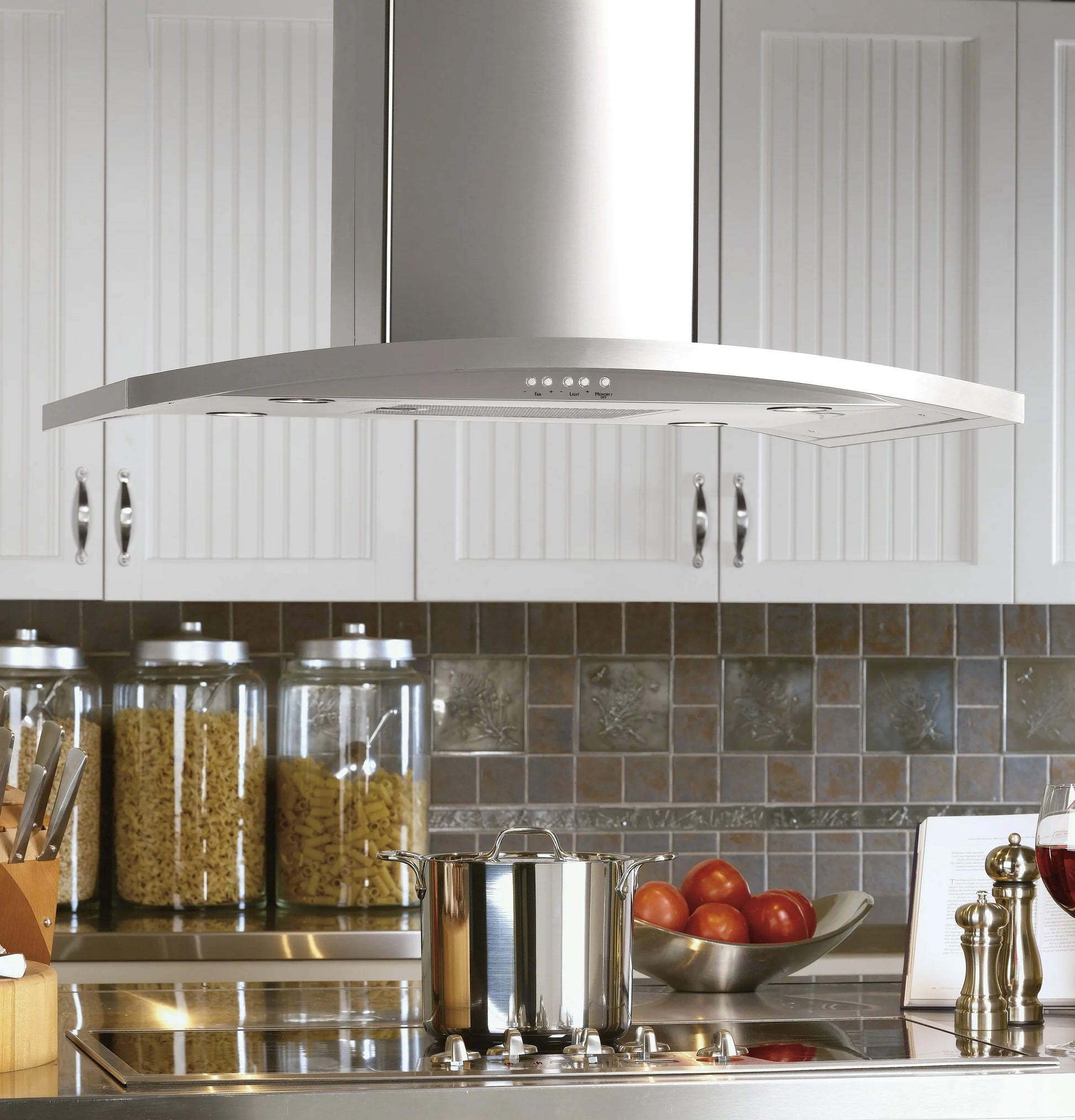 Stainless steel island-mount range hood above cooktop in kitchen with white cabinets and tiled backsplash