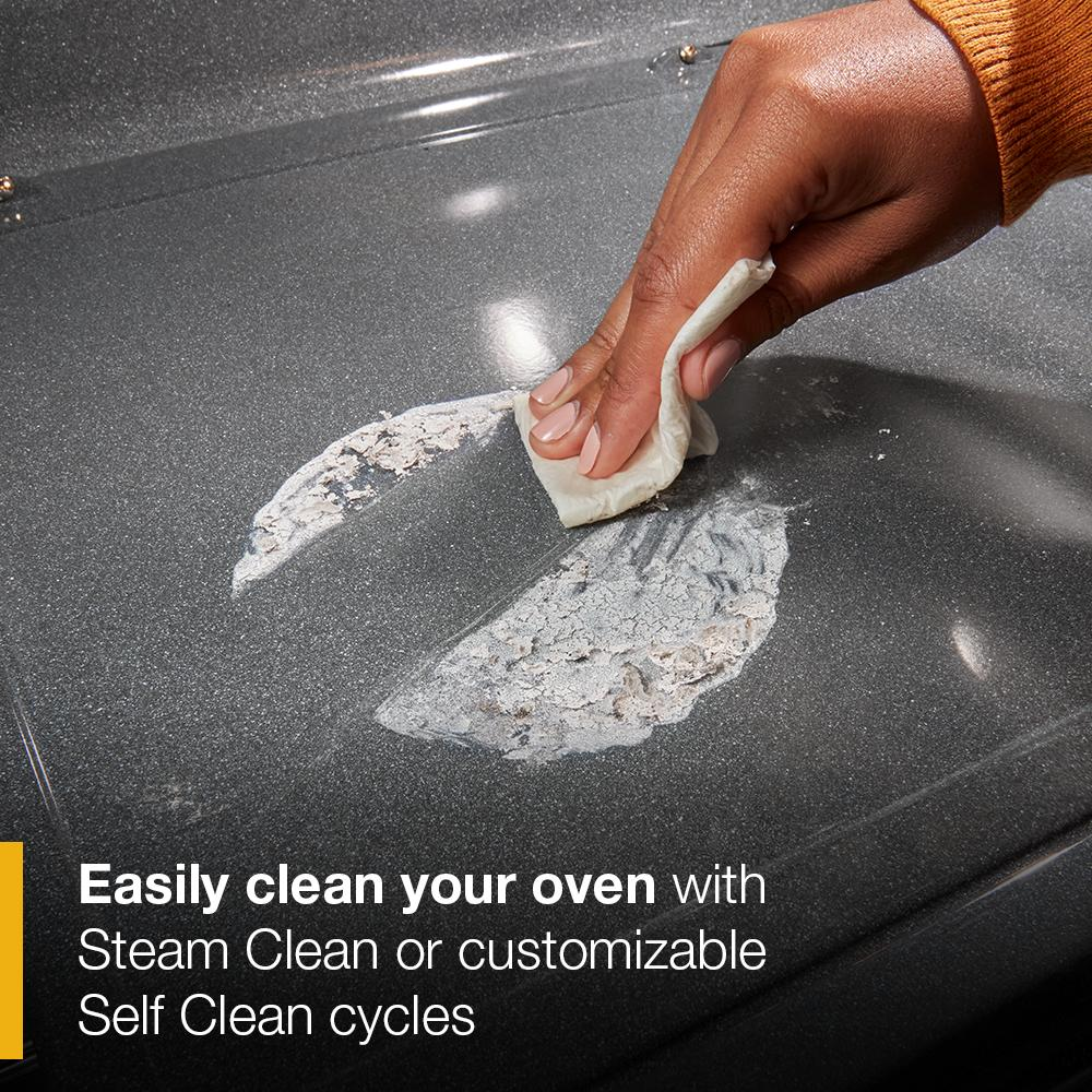 Hand wiping peeling residue from gray oven interior surface demonstrating easy cleaning feature