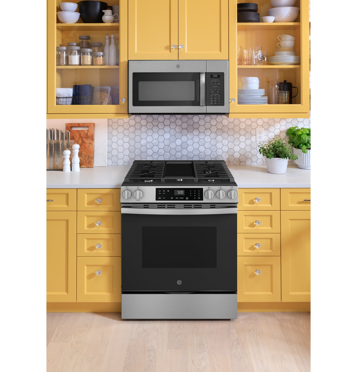 Stainless steel slide-in gas range with front controls in a bright kitchen featuring yellow cabinets and hex tile backsplash