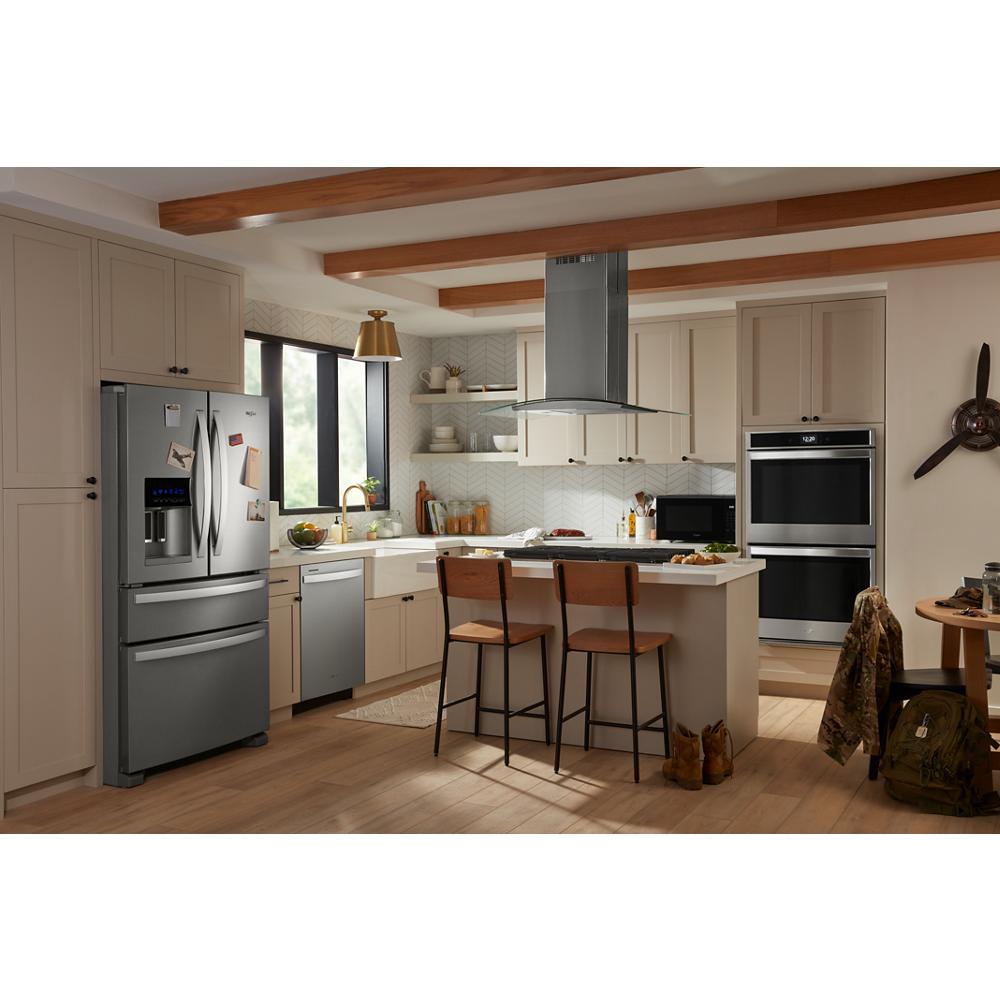 Modern kitchen with stainless steel curved glass island range hood, beige cabinets, and wood ceiling beams near dining area.