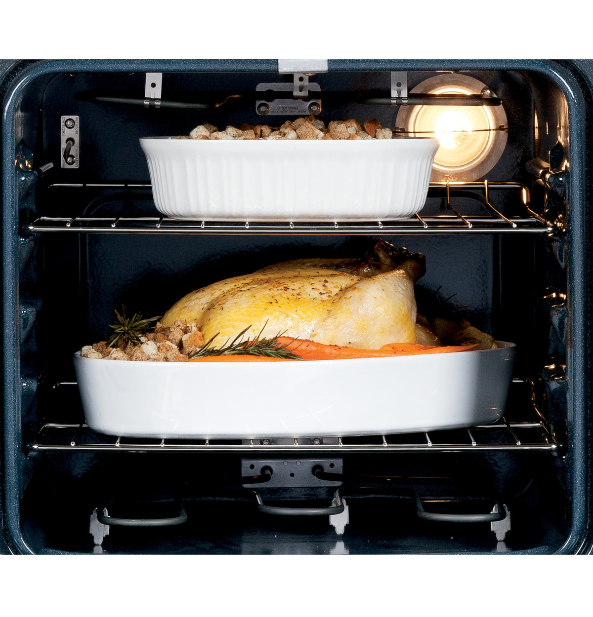 Interior view of electric wall oven with roasted chicken and casserole dishes on two racks from kitchen appliances collection
