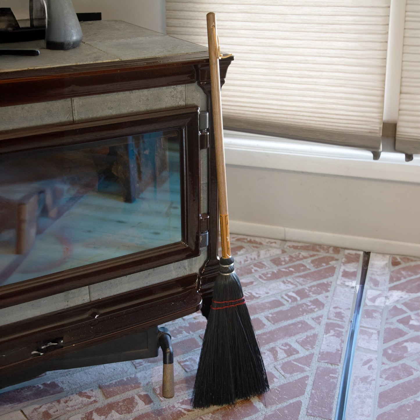 Black bristle broom with natural wood handle leaning against a fireplace in a home cleaning setting under $50 collections