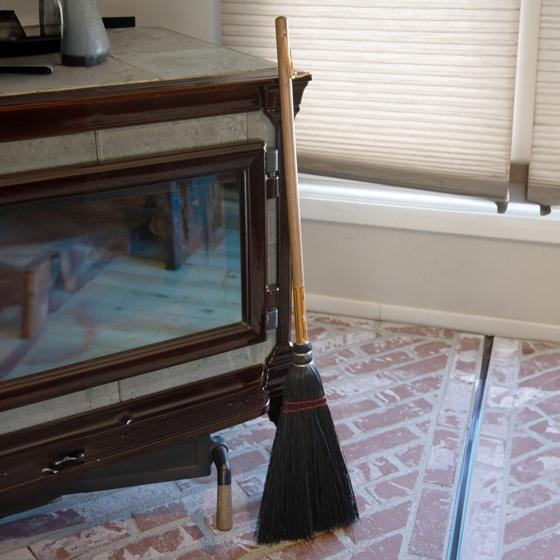 Black bristle broom with natural wood handle leaning against a fireplace in a home cleaning setting under $50 collections