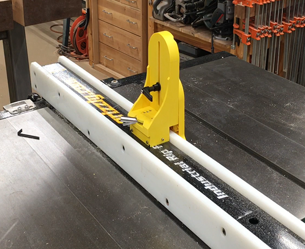 Yellow vertical featherboard with adjustable locking knob on white and black guide rail for saw tool accessories