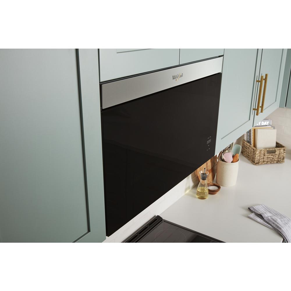 Black flush mount microwave with stainless steel trim installed between green kitchen cabinets and white countertop surface