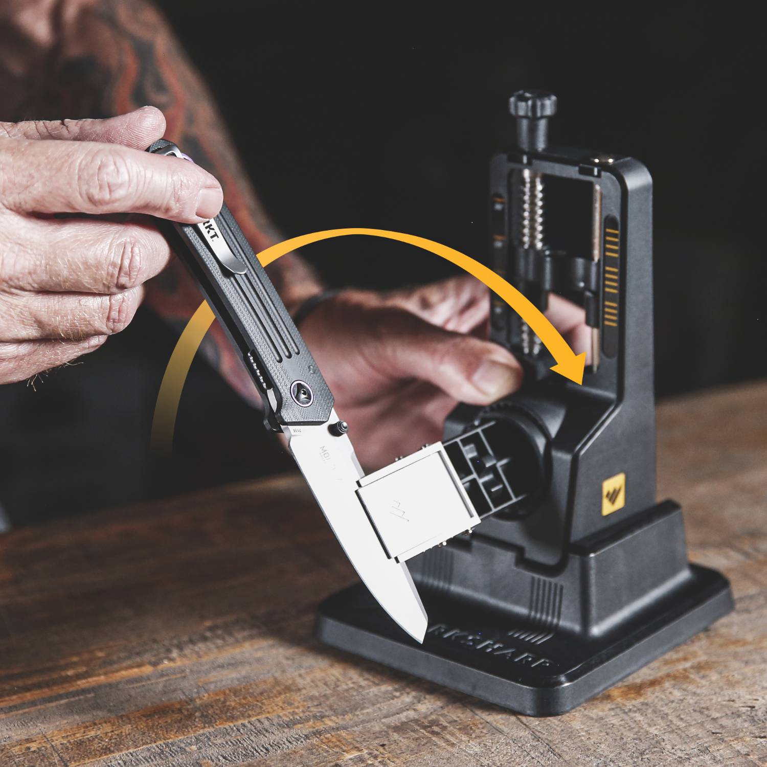 Man using adjustable sharpener to hone folding knife blade on wooden table for kitchenware and hand tools maintenance