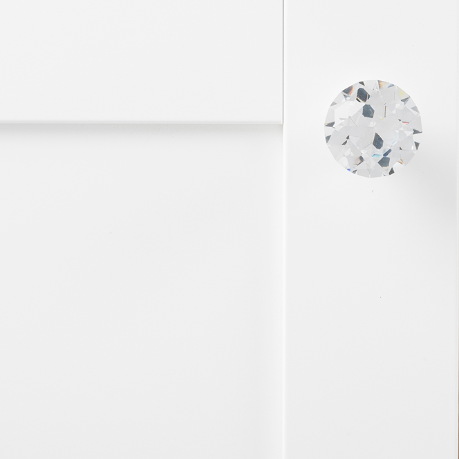 Faceted glass knob with chrome base attached to white cabinet door for furniture hardware and home improvement projects