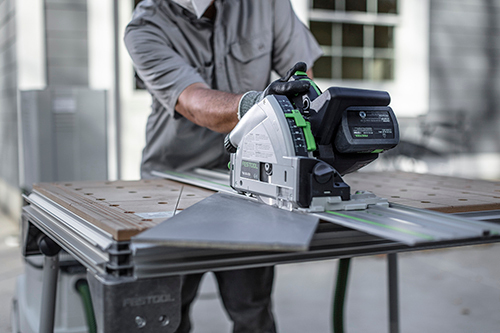 Person operating Festool cordless track saw with guide rail on workbench in workshop for precise wood cutting