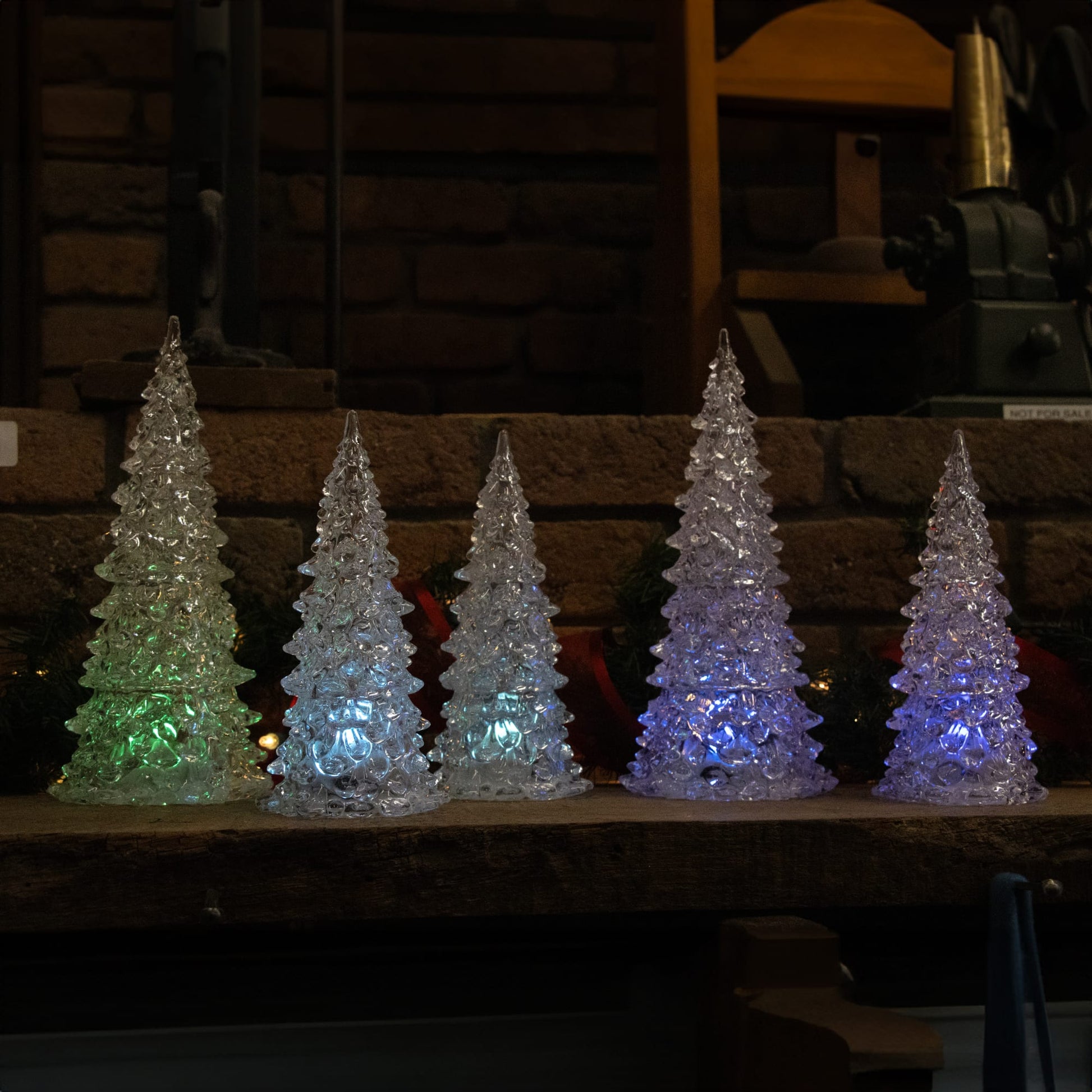 Five translucent light-up trees glowing in multicolor hues on a rustic wooden surface for cozy home decor