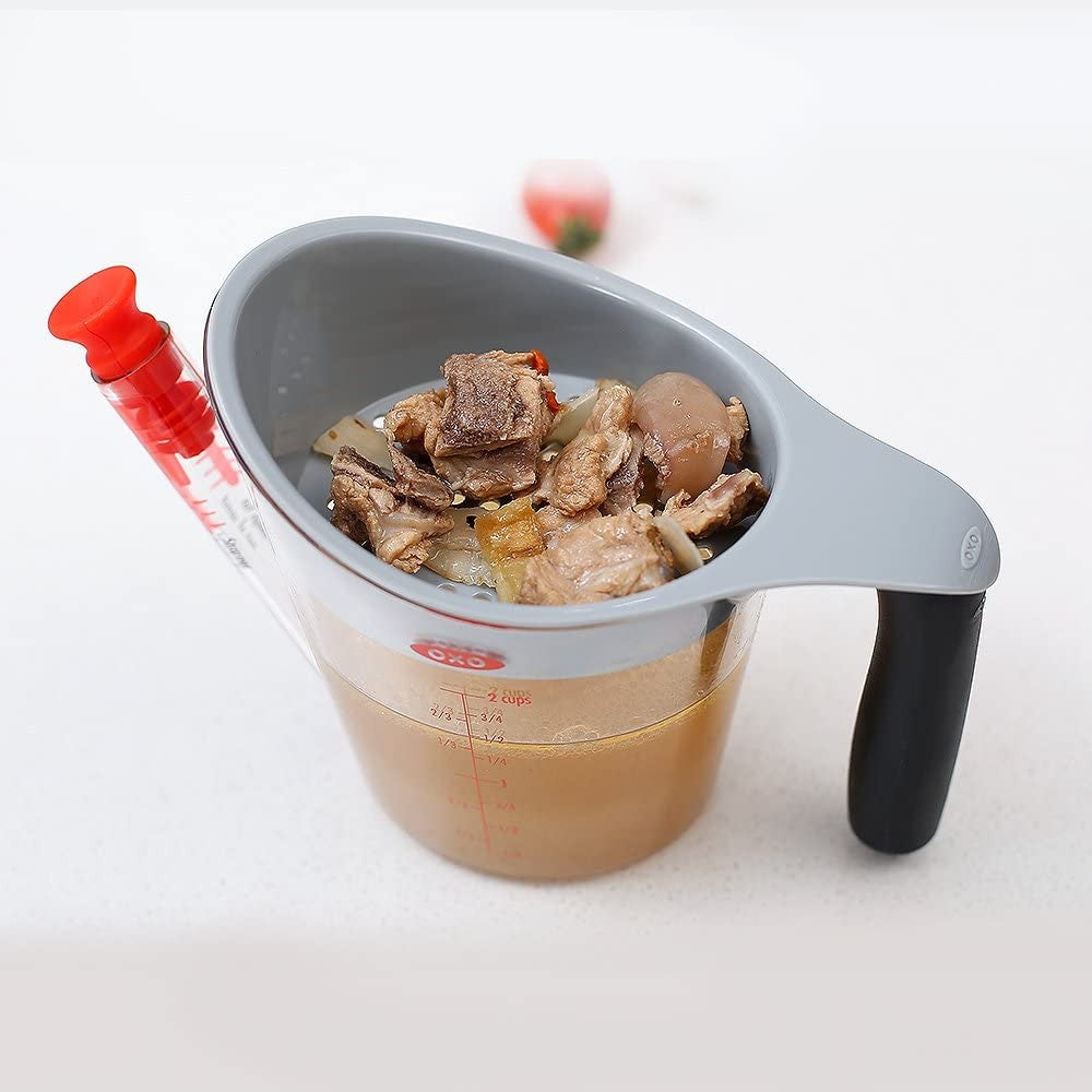 Clear measuring cup with gray strainer pouring broth from cooked meat with black handle for kitchen gadgets collections