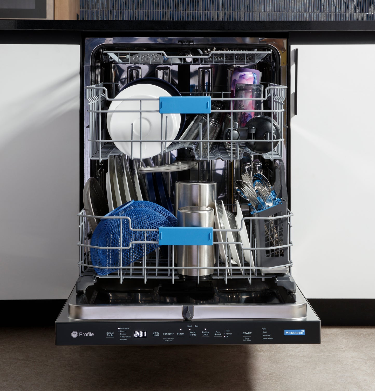 Open stainless interior dishwasher with top control panel, loaded with dishes, utensils, and kitchenware in modern kitchen