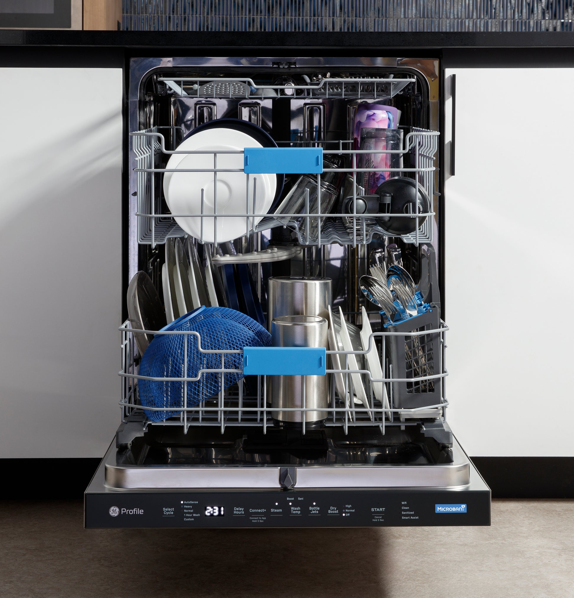 Open stainless interior dishwasher with top control panel, loaded with dishes, utensils, and kitchenware in modern kitchen