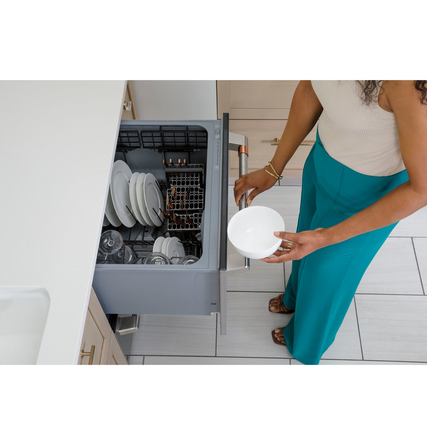 Upper drawer of dishwasher opened with white plates and bowls inside in a modern kitchen setting for home improvement
