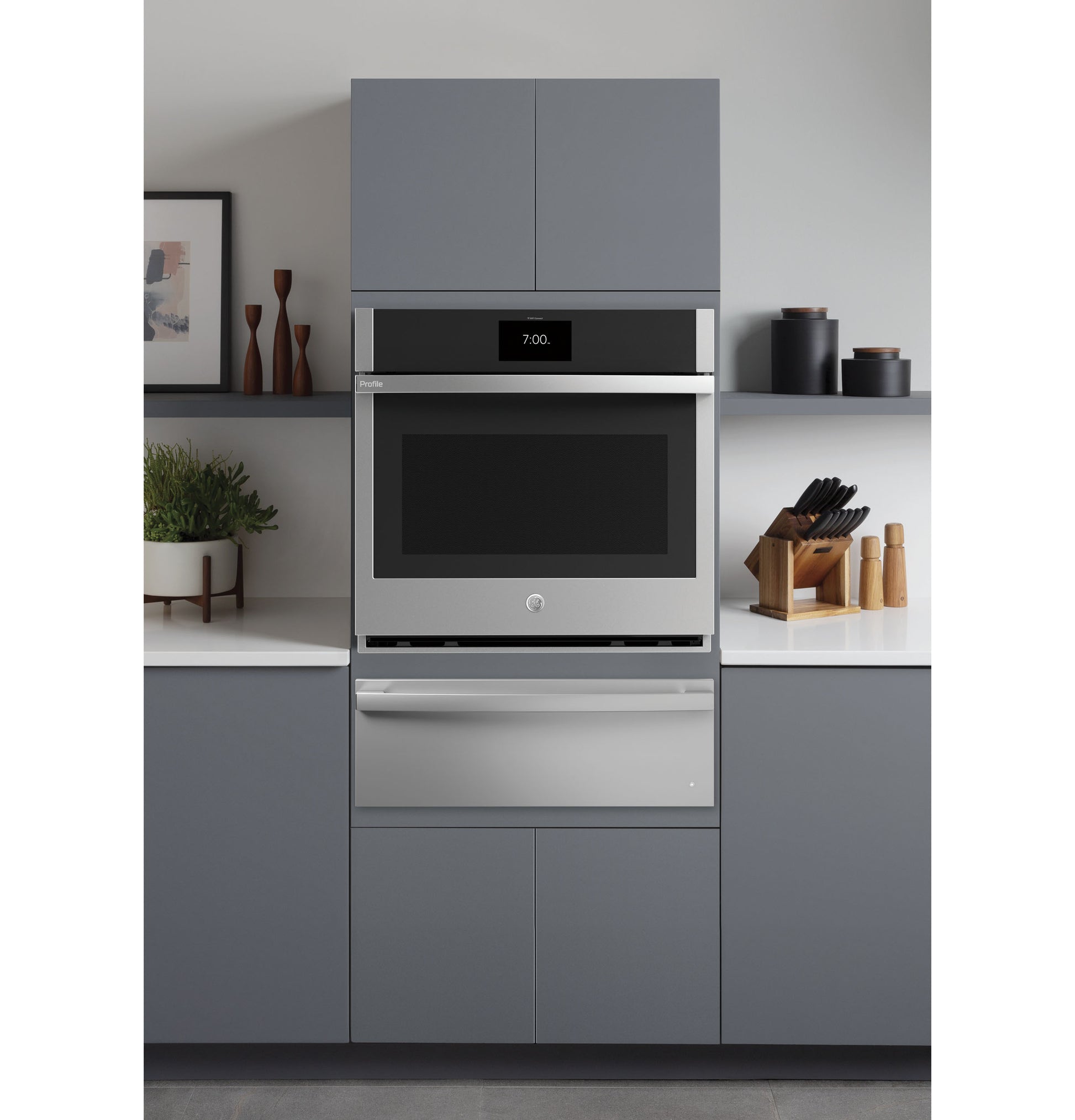 Built-in stainless steel warming drawer installed below a wall oven in a modern kitchen setting