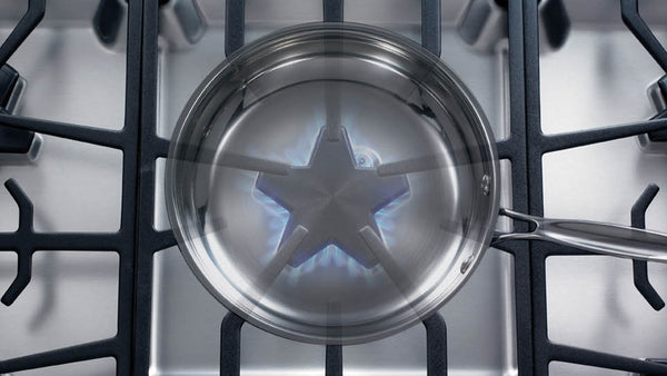 Stainless steel gas cooktop burner ignited under a pan with continuous grates in kitchen appliances collection